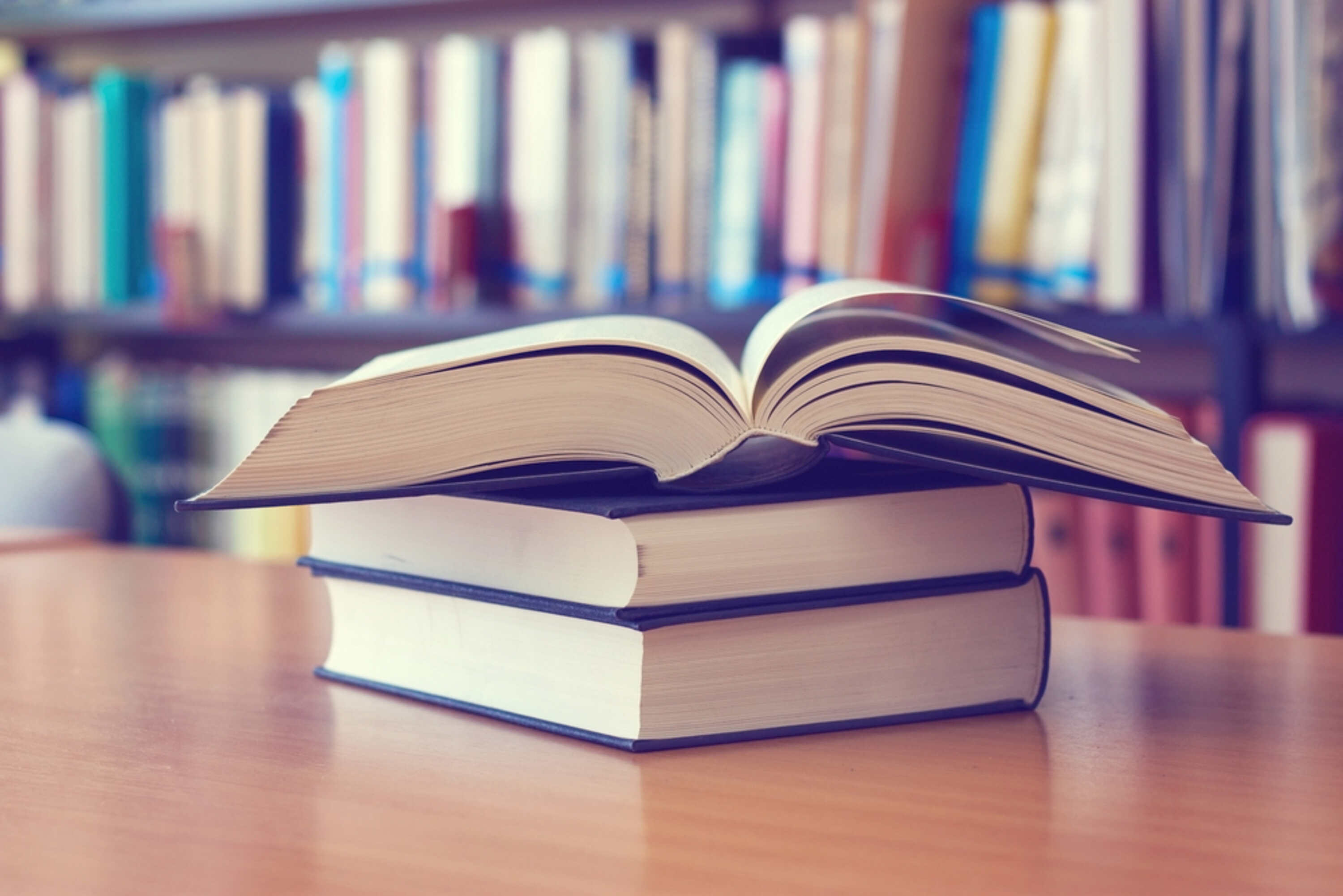 Bücherstapel auf einem Holztisch. Oberstes Buch ist aufgeschlagen.